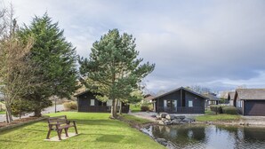 Zona de cabañas junto al lago con un banco, cabañas de madera y un estanque.