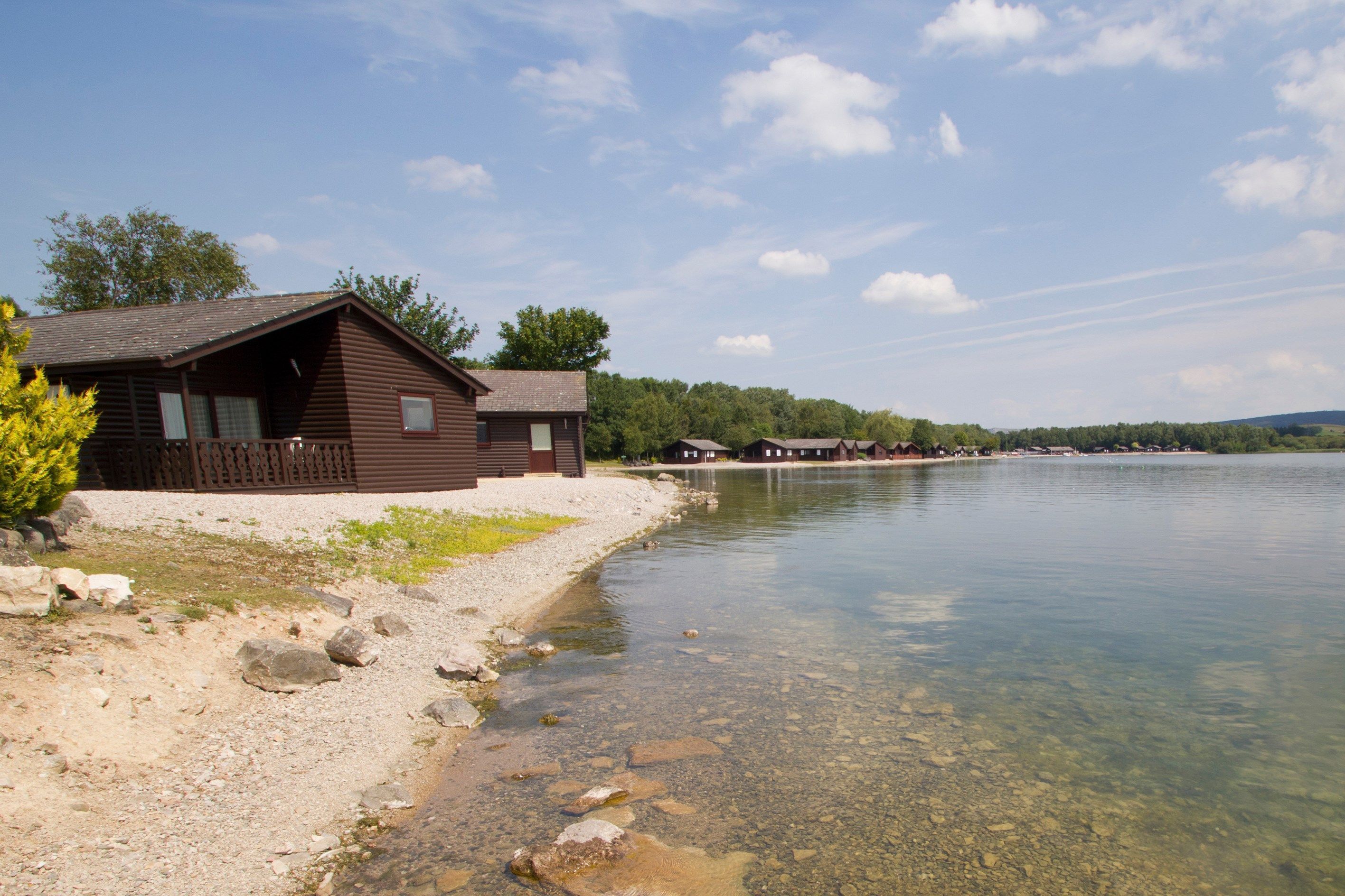A cabin by a lake with clear water, a gravel path, and a wooden deck.