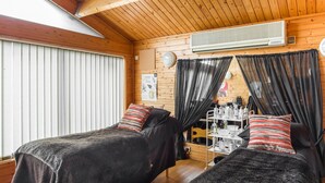 Una habitación acogedora con dos camas, techo de madera, aire acondicionado potente y ventana con persianas.