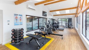 Un gimnasio con equipamiento de ejercicio, amplias ventanas y vigas de madera.