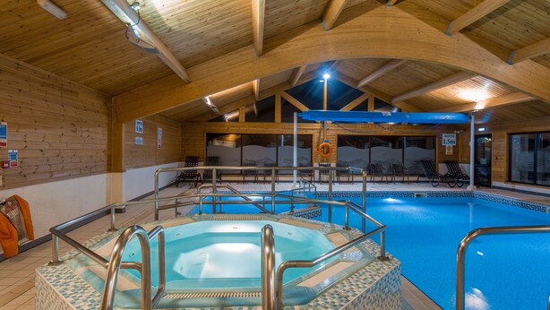Una piscina interior con jacuzzi, vigas de madera y sillones de descanso.