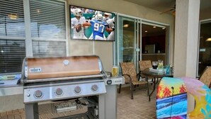 Un barbecue, des sièges d’extérieur et un téléviseur diffusant un match de football.
