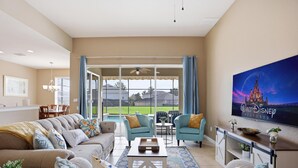 Un salon avec un canapé, des fauteuils, une table basse, un téléviseur et une grande fenêtre avec des rideaux.