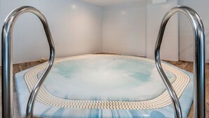 Un jacuzzi con barandillas metálicas, rodeado por un muro blanco y suelo de madera.