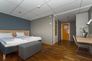 A hotel room with a bed, a desk with a laptop, a chair, and a small table with a plant. - Hotel Aurora (Vagan)