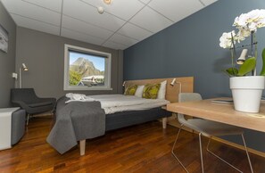 Une chambre d’hôtel moderne équipée d’un lit, d’un bureau, d’une chaise, d’une fenêtre donnant sur la montagne et d’une orchidée en pot.