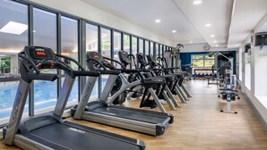 A gym with multiple treadmills, weight machines, and a large window providing a view of the outdoors.
