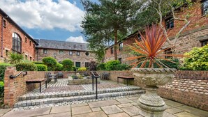 A courtyard with stone flooring, a central seating area with benches, and a large decorative planter. - Modern 1-Bed Apartment | Near Lancaster | Sleeps 4 (Lancaster)