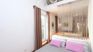 Een slaapkamer met een bed, een raam met gordijnen, een bank met kussens en uitzicht op de omgeving.