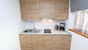 Een kleine keuken met houten kastjes, een roestvrijstalen spoelbak, een waterkoker en een koffiezetapparaat.