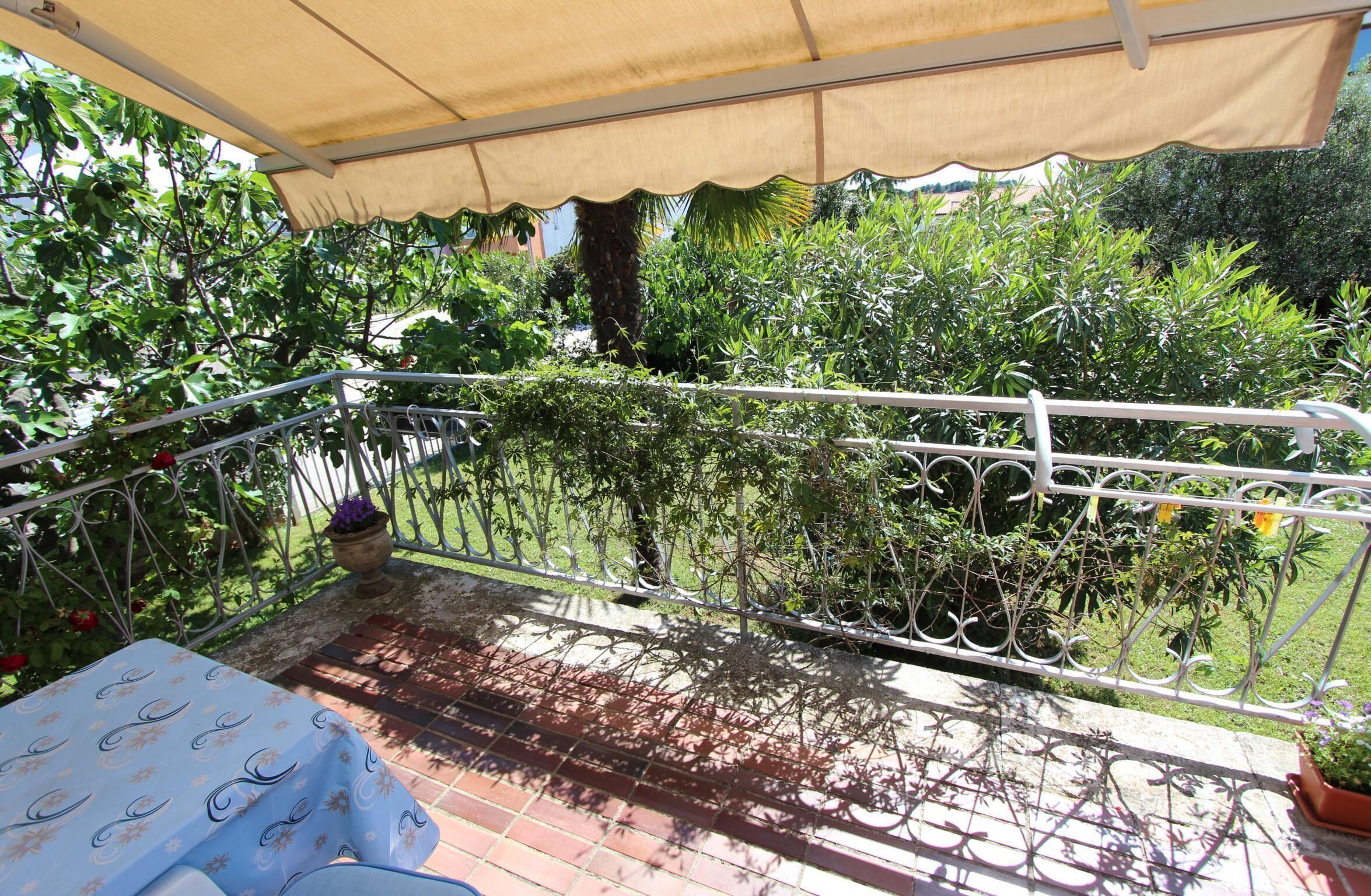 Ein überdachter Balkon mit Metallgeländer, Blumentöpfen und einem Tisch mit Tischdecke.
