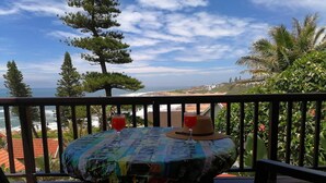 A table with a colorful tablecloth, two glasses of red drink, and a straw hat on a balcony overlooking a beach and ocean. - All the Tides - Hi Tide (Margate)