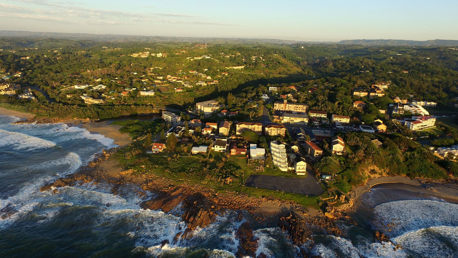 An aerial view of a coastal town with residential buildings, a beach, and rocky coastline.