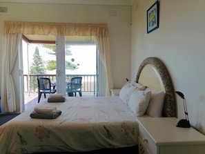 A bedroom with a bed, a nightstand, a chair, and a view of the outside balcony. - All the Tides - Hi Tide (Margate)