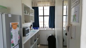 A compact kitchen with a refrigerator, microwave, and sink. Shelves are above the counter, and a trash bin is visible. - All the Tides - Hi Tide (Margate)