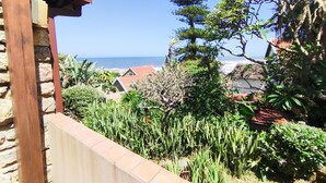 A coastal view with a stone wall, lush greenery, and a clear blue sky. - All the Tides - Lo Tide (Margate)