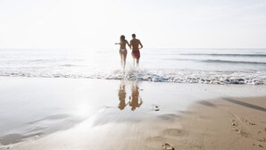 To personer går på en sandstrand med bølger i baggrunden.