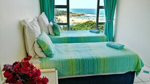 Un dormitori amb dos llits, vistes a la platja i un ram de flors vermelles.