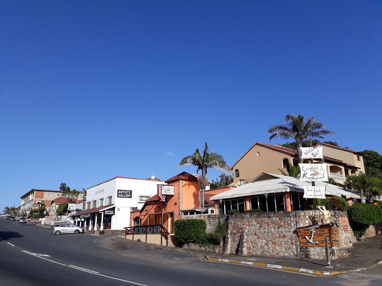 A street view with buildings, including a restaurant with outdoor seating and a sign for a gallery.