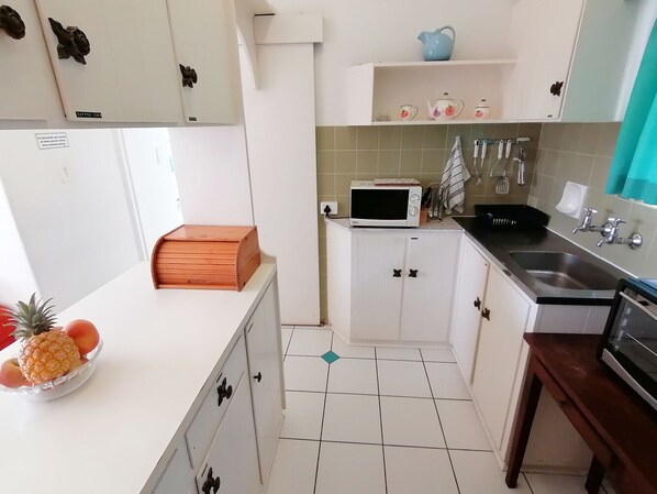 A compact kitchen with white cabinets, a microwave, a sink, and a wooden countertop. - Claridges 303 (Margate)
