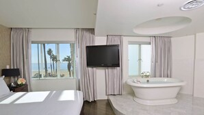 Quarto de hotel com cama, televisão, banheira e vista para a praia.
