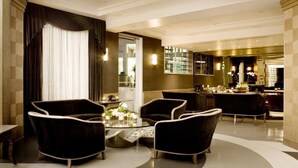 Um lobby de hotel moderno com uma mesa redonda, cadeiras estofadas escuras e uma mesa de centro de vidro.