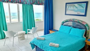 A bedroom with a bed, a chair, a small table, and a view of the sea through the window.