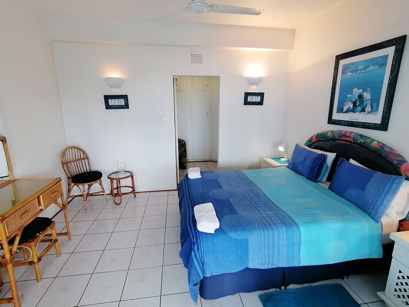 A bedroom with a bed, a desk, two chairs, a small table, and a door.
