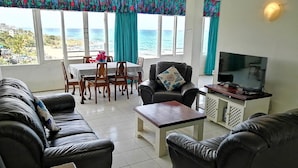A living room with a sofa set, a coffee table, a TV stand, and a dining area with chairs and a table. - Claridges 404 (Margate)