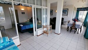 A hotel room with a balcony, a dining area, and a bed with a blue bedspread. - Claridges 404 (Margate)