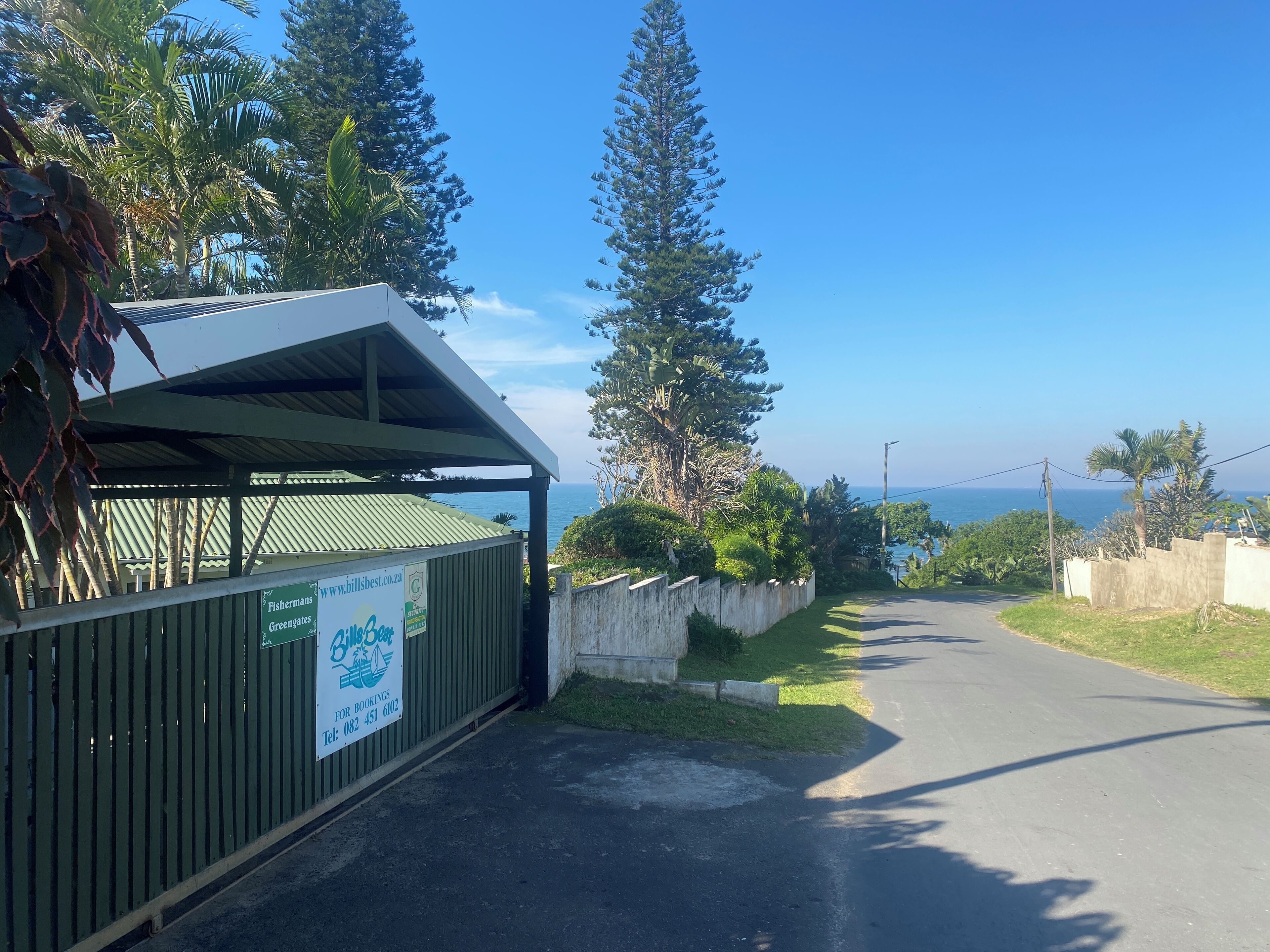 A coastal road with a covered structure, a signboard advertising Fishermans Greenates, and a view of the sea.