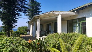 A white building with a covered porch and large windows. - Greengates Cottage (Port Edward)