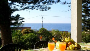 A table with a fruit bowl and two glasses of orange juice, overlooking a coastal view. - Greengates Cottage (Port Edward)