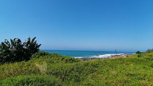 A coastal landscape with a beach, ocean, and lush greenery. - Greengates Cottage (Port Edward)