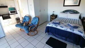 Une chambre comprenant un lit, une chaise, une table de chevet et un coin cuisine.