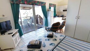 Une chambre comprenant un lit, une télévision, une petite table, une chaise et une porte coulissante donnant sur un espace extérieur avec une table et des chaises.