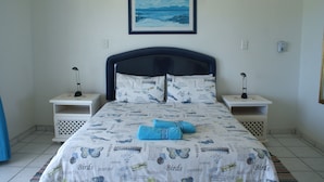 A neatly made bed with a printed bedspread, two bedside tables with lamps, and a framed picture on the wall. - Rosscarbery 3 (Margate)