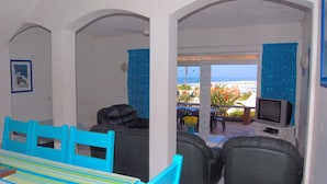A room with a dining table and chairs, a sofa, a television, and a view of the ocean. - Rosscarbery 3 (Margate)