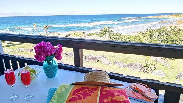 A balcony with a view of the ocean, a table with a vase of flowers, two glasses of red drink, and a beach towel. - Rosscarbery 5 (Margate)