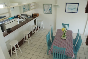Cocina compacta con gabinetes blancos, estufa y lavamanos. Hay dos taburetes blancos y una mesa con un centro de mesa floral.