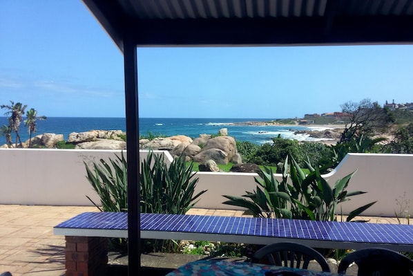 Un patio con una mesa de energía solar, con vista a una costa rocosa y vistas al océano y edificios distantes.