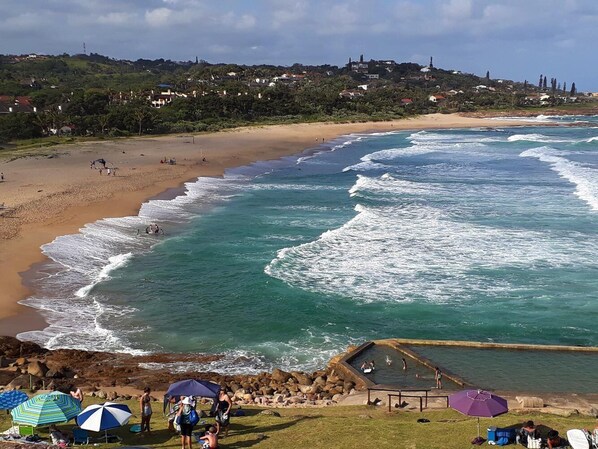 A coastal beach with waves, umbrellas, and people.