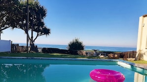 A swimming pool with a pink inflatable ring, surrounded by a wooden fence, palm trees, and a view of the ocean. - Southern Comfort - On the Pool (Margate)
