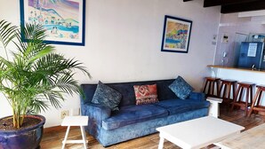 A living room with a blue sofa, a white coffee table, and a potted plant. There are two framed paintings on the wall. - Southern Comfort - On the Pool (Margate)