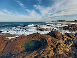 A rocky shoreline with waves crashing against the rocks and a clear sky.