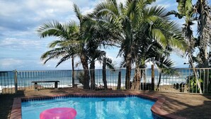 Una piscina amb un anell inflable rosa, envoltada de palmeres i vista a l'oceà.