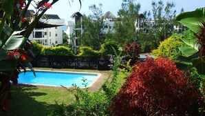 A swimming pool surrounded by lush greenery and a fence, with buildings in the background. - Weavers Nest (Margate)