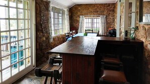 Un espace repas avec une longue table en bois, des murs en pierre et de grandes fenêtres.