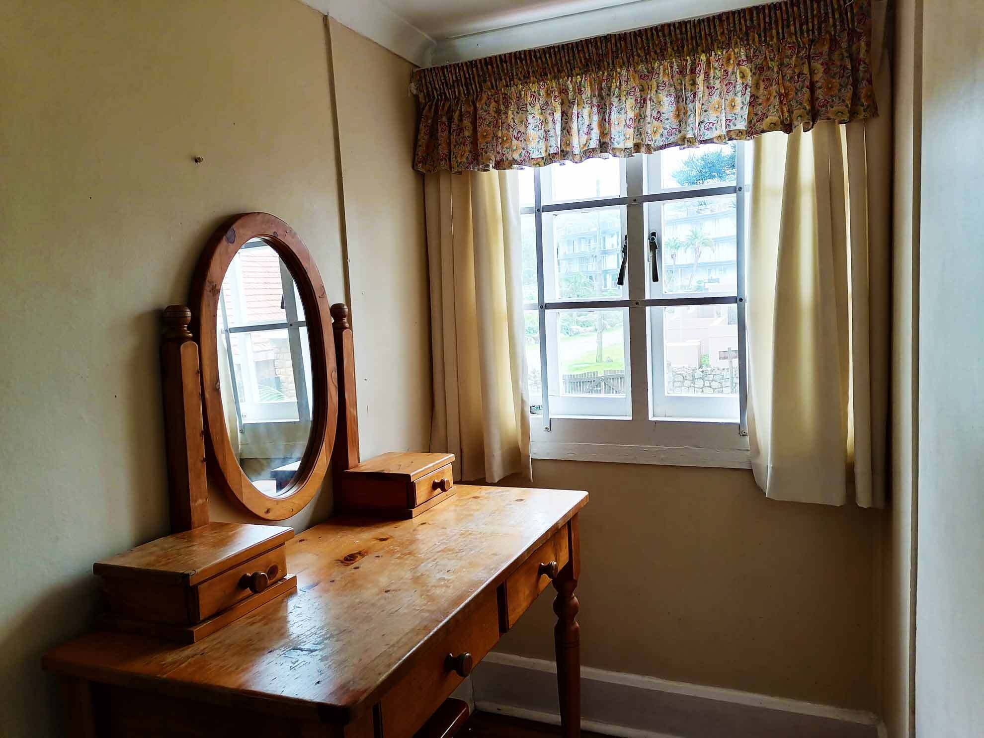 A wooden dresser with a mirror and drawers, a window with curtains, and a view of the outside.