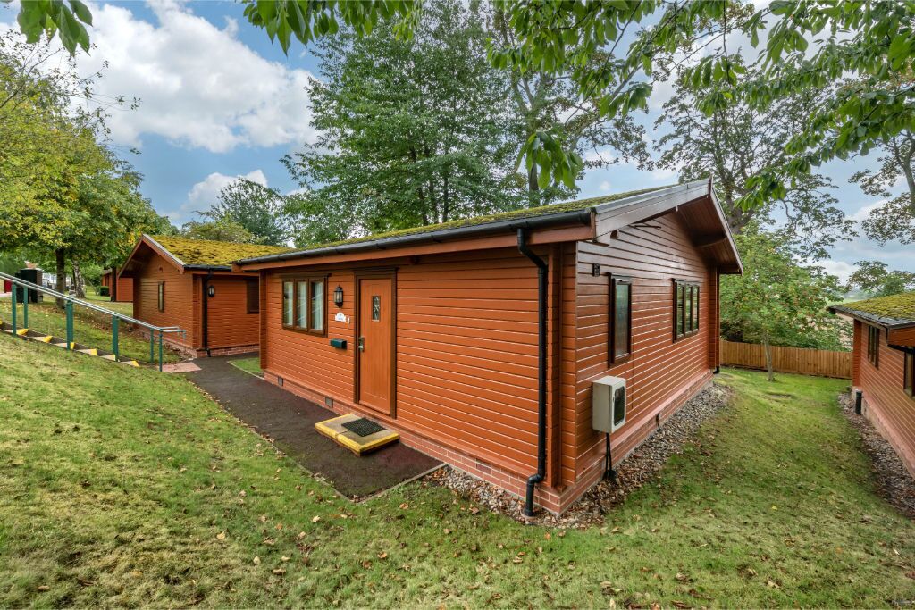 Une cabane en bois avec un porche, un petit jardin devant et un escalier menant à l’entrée.